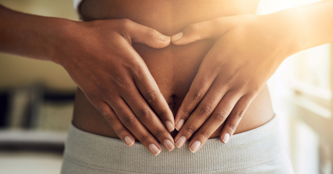 A close up image of a woman's abdomen with her hands over her stomach in a heart shape emphasizing how peptides like BPC-157 can help with gut issues like bloating and discomfort