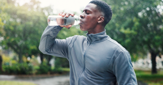 A close up photo of an athletic man drinking water from a water bottle emphasizing the importance of hydration and water intake while taking peptide therapyi